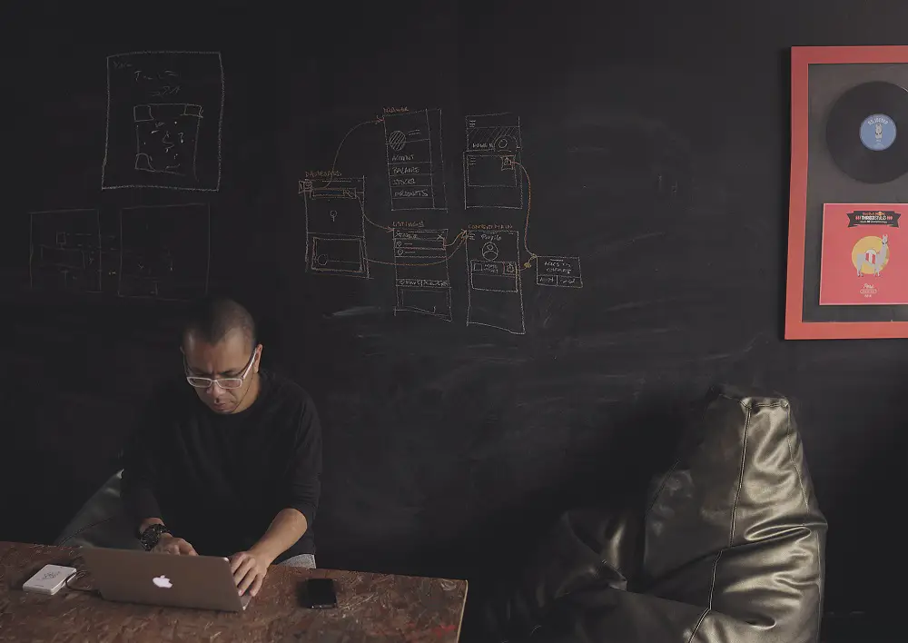 architect wearing black sitting on a black bean bag chair against a chalk wall