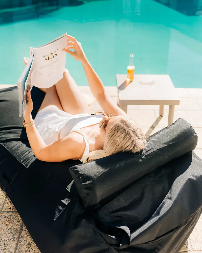 girl with magazine sitting by the pool on the best bean bag chair in black